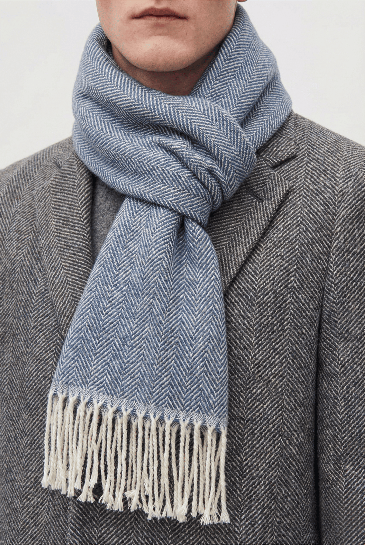 Écharpe à carreaux et chevrons bleus, à franges écrues, portée avec un manteau gris
