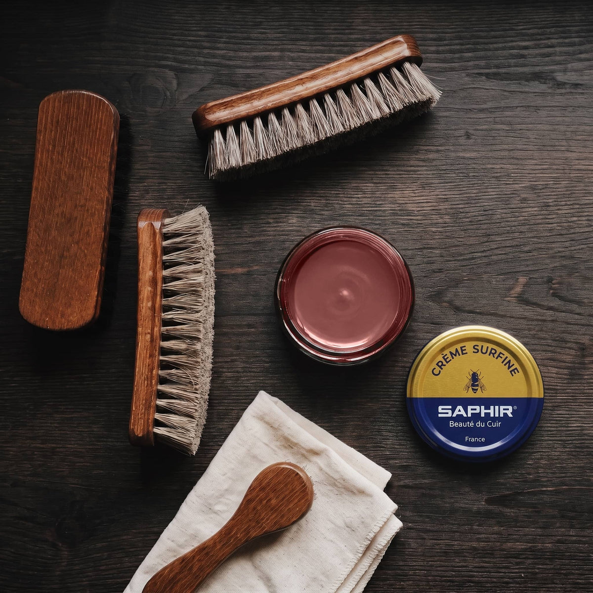 Crème Surfine Saphir Acajou en pot ouvert, avec des brosses en crin et une chamoisine, vue de dessus
