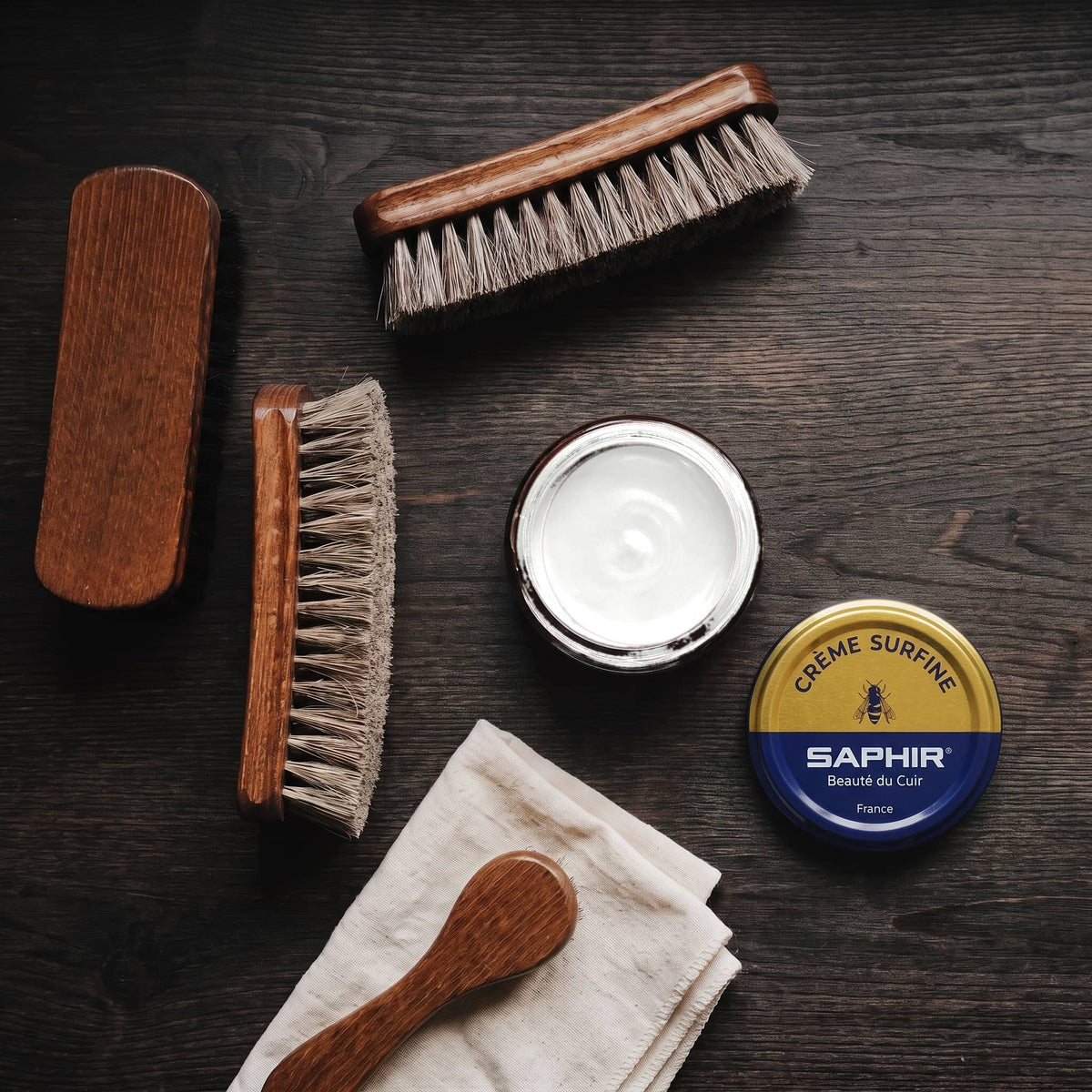 Crème Surfine Saphir Blanc en pot ouvert, avec des brosses en crin et une chamoisine, vue de dessus
