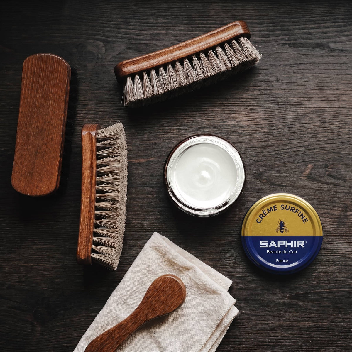 Crème Surfine Saphir Blanc cassé en pot ouvert, avec des brosses en crin et une chamoisine, vue de dessus