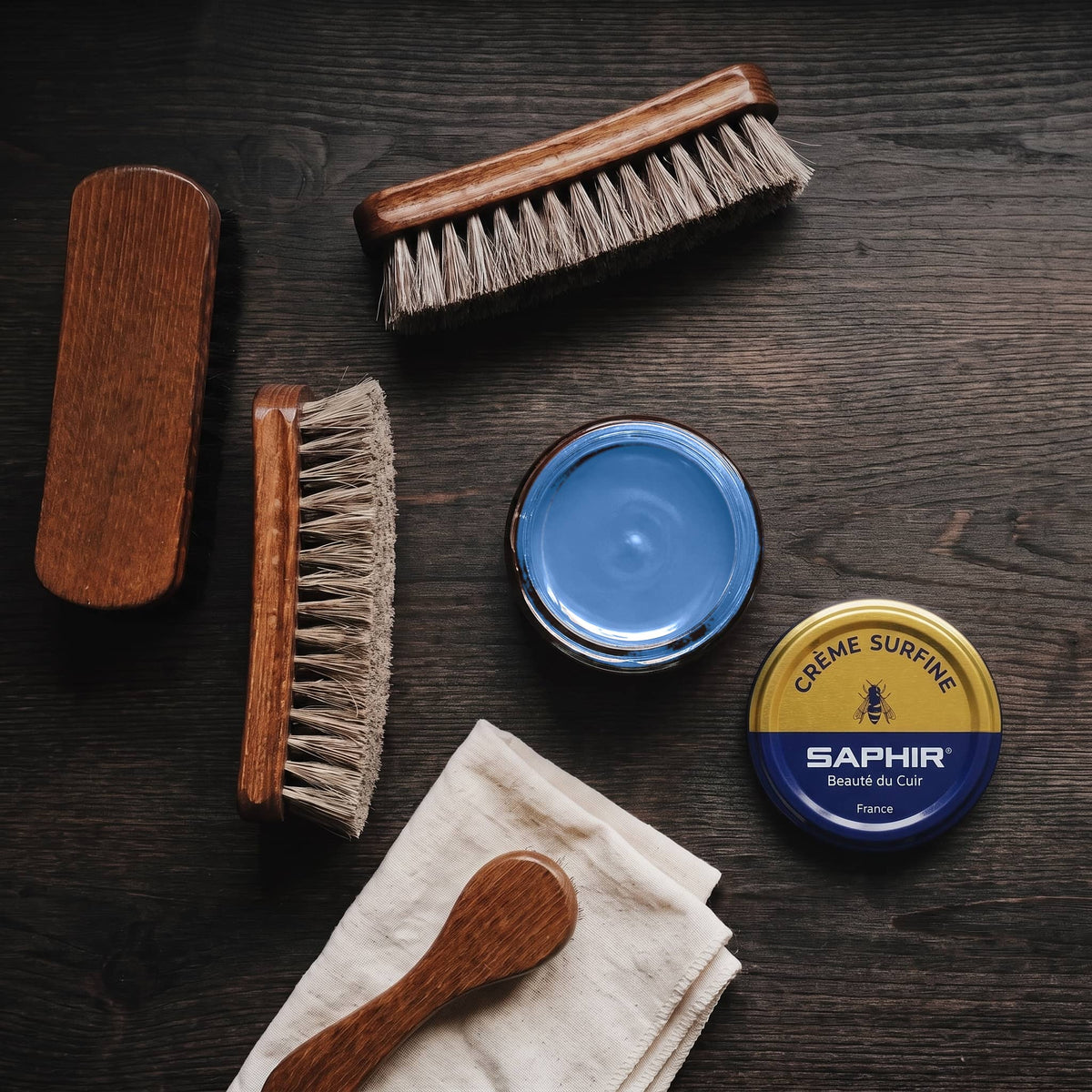 Crème Surfine Saphir Bleu azur en pot ouvert, avec des brosses en crin et une chamoisine, vue de dessus