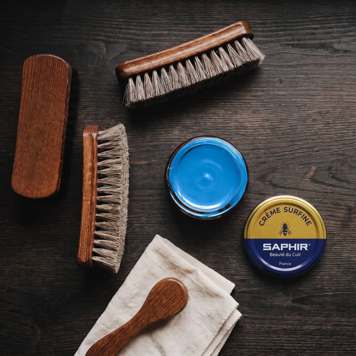 Crème Surfine Saphir Bleu iris en pot ouvert, avec des brosses en crin et une chamoisine, vue de dessus