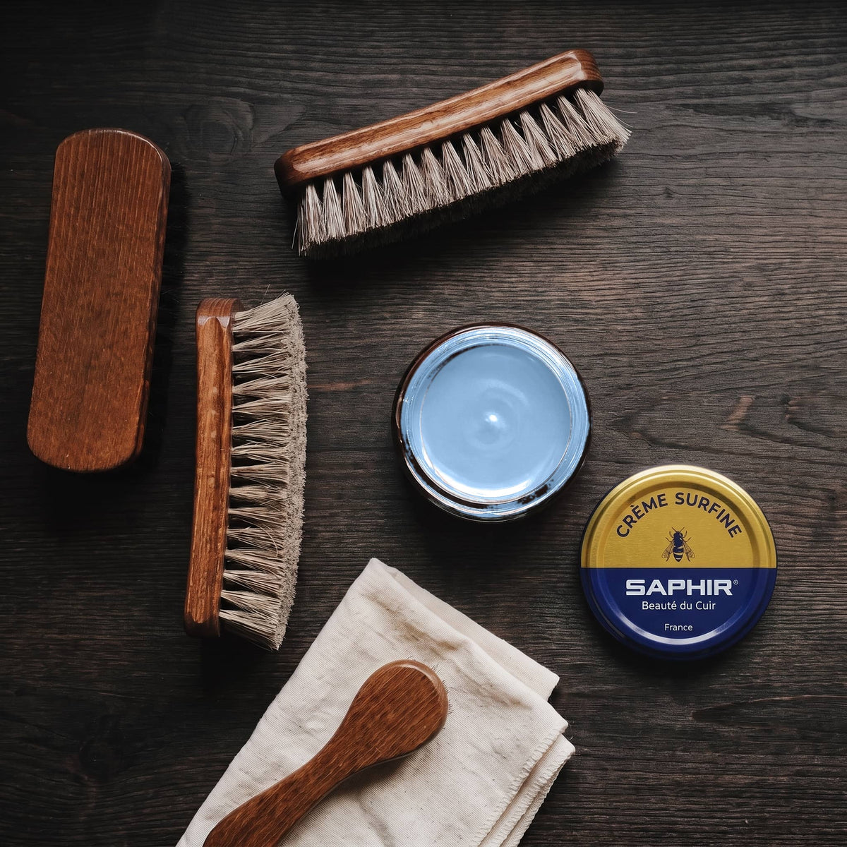 Crème Surfine Saphir Bleu jean en pot ouvert, avec des brosses en crin et une chamoisine, vue de dessus
