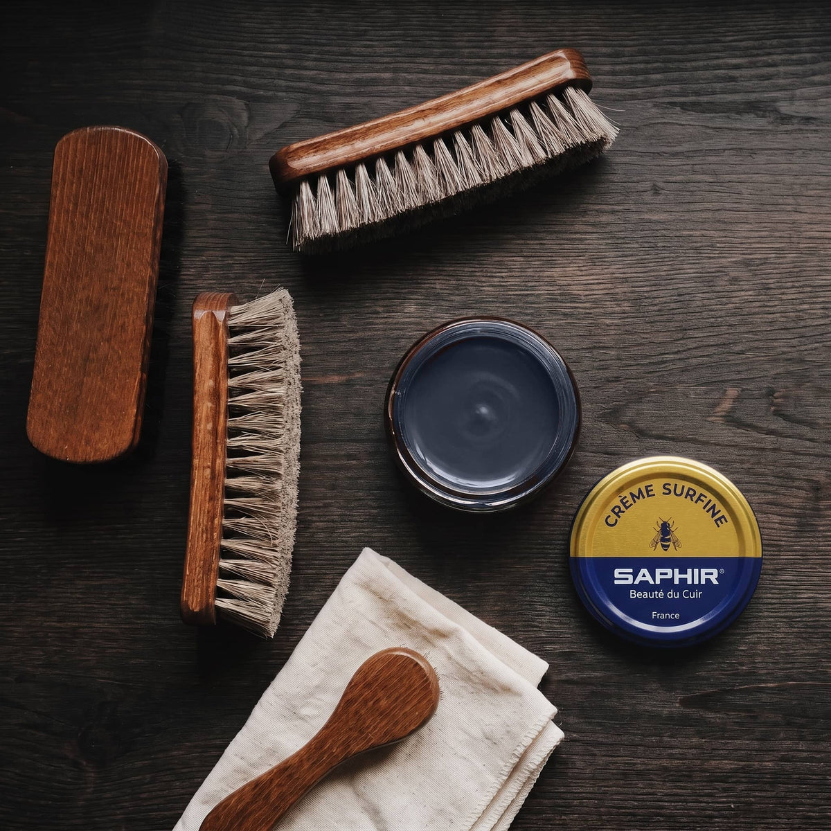 Crème Surfine Saphir Bleu marine en pot ouvert, avec des brosses en crin et une chamoisine, vue de dessus