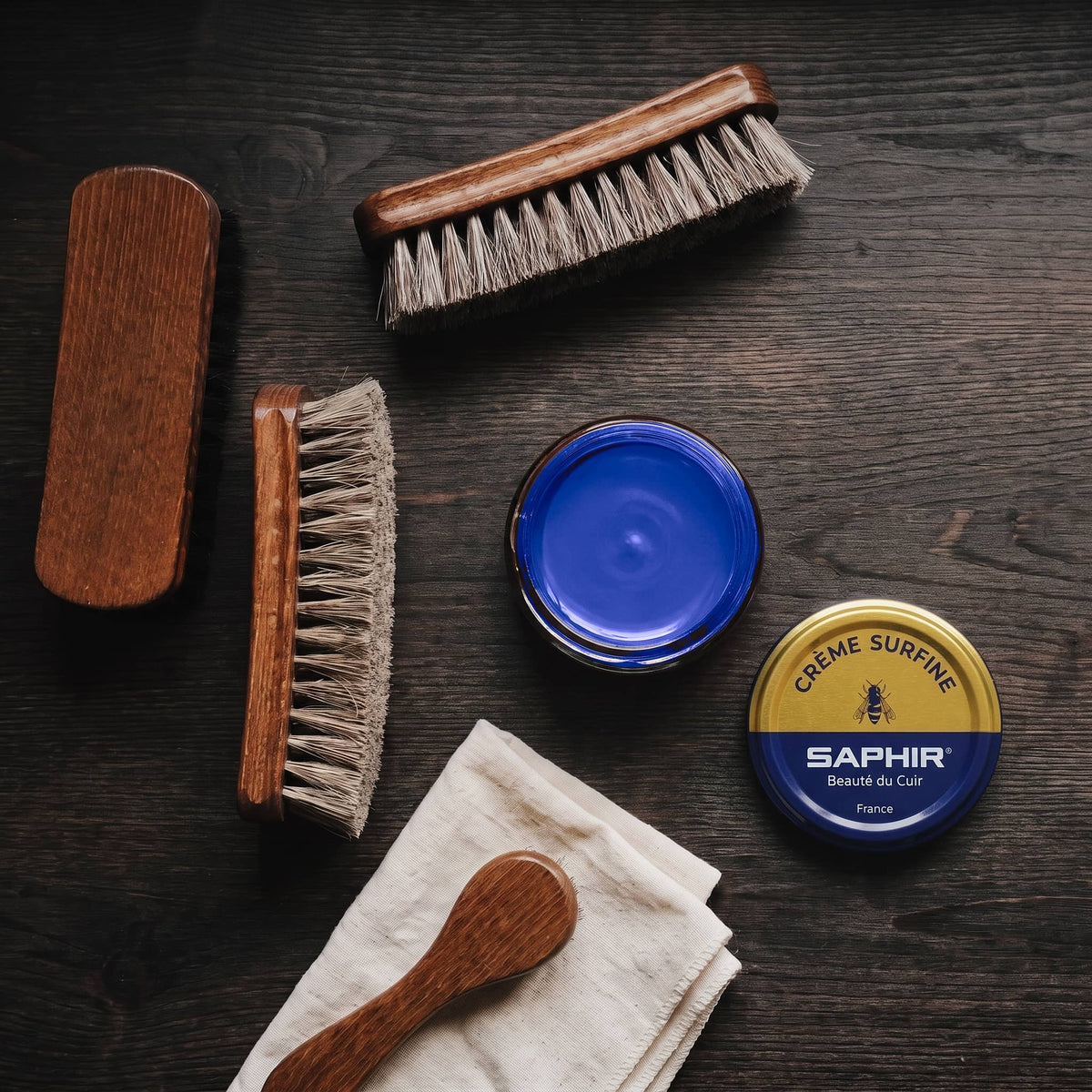 Crème Surfine Saphir Bleu océan en pot ouvert, avec des brosses en crin et une chamoisine, vue de dessus