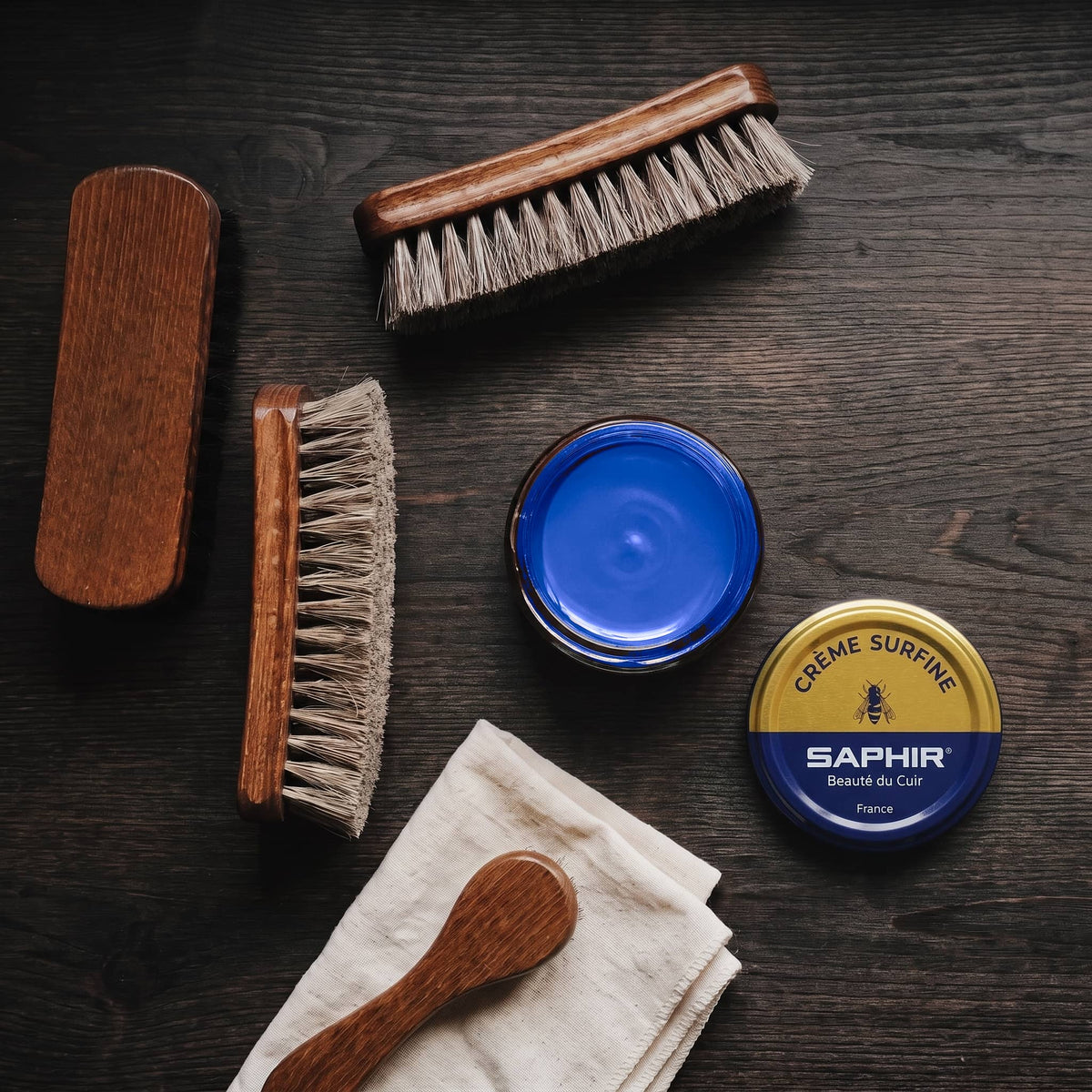 Crème Surfine Saphir Bleu Saphir en pot ouvert, avec des brosses en crin et une chamoisine, vue de dessus