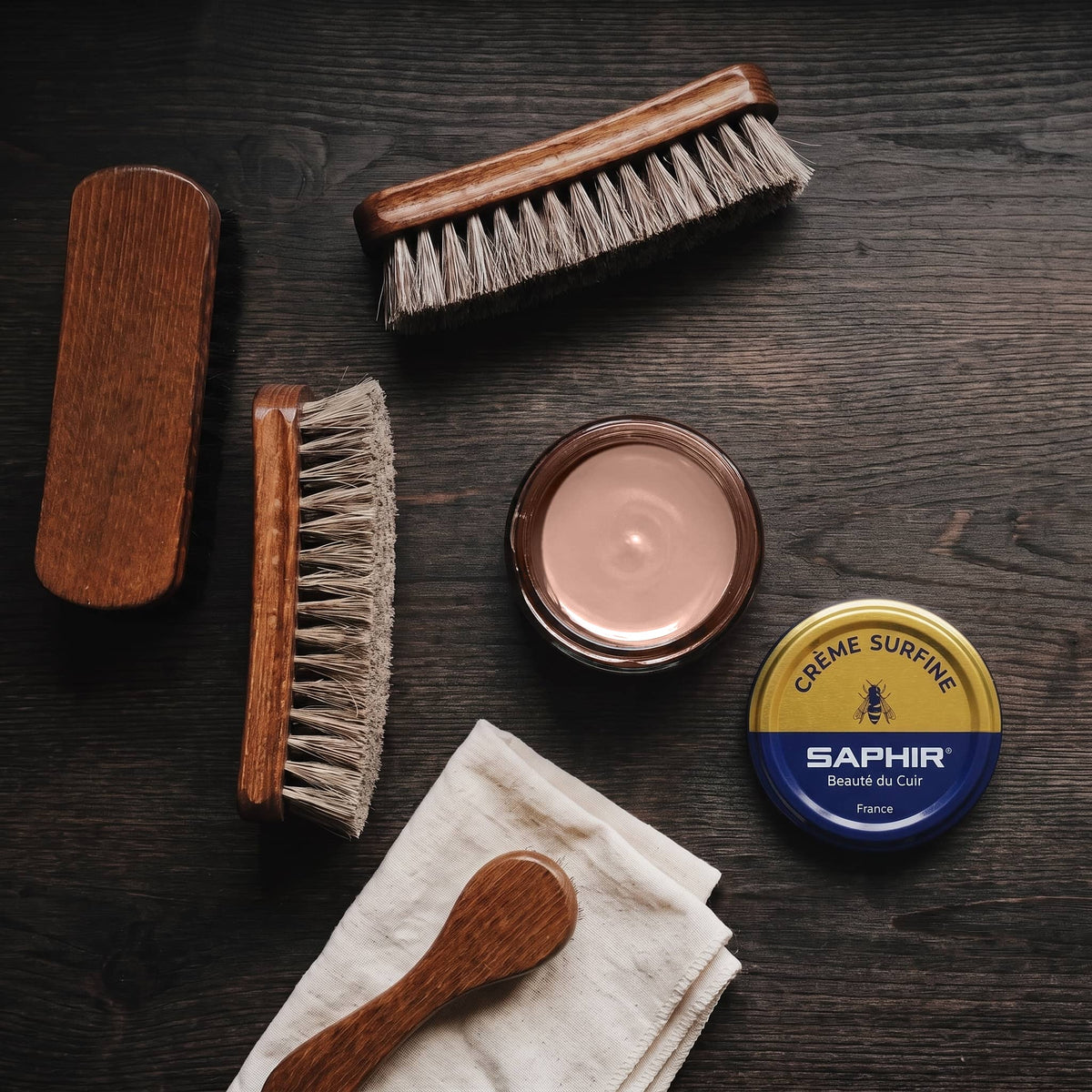 Crème Surfine Saphir Brun Rosé en pot ouvert, avec des brosses en crin et une chamoisine, vue de dessus
