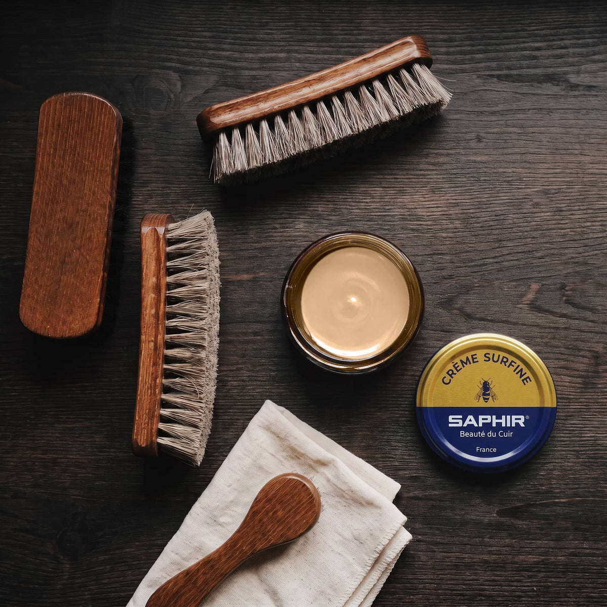 Crème Surfine Saphir Chamois en pot ouvert, avec des brosses en crin et une chamoisine, vue de dessus