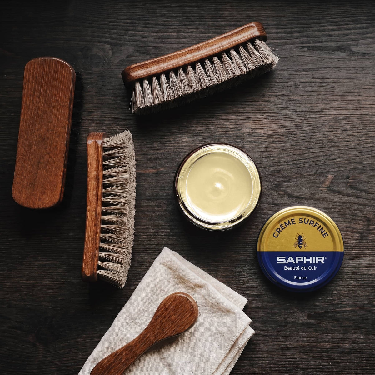 Crème Surfine Saphir Ficelle en pot ouvert, avec des brosses en crin et une chamoisine, vue de dessus