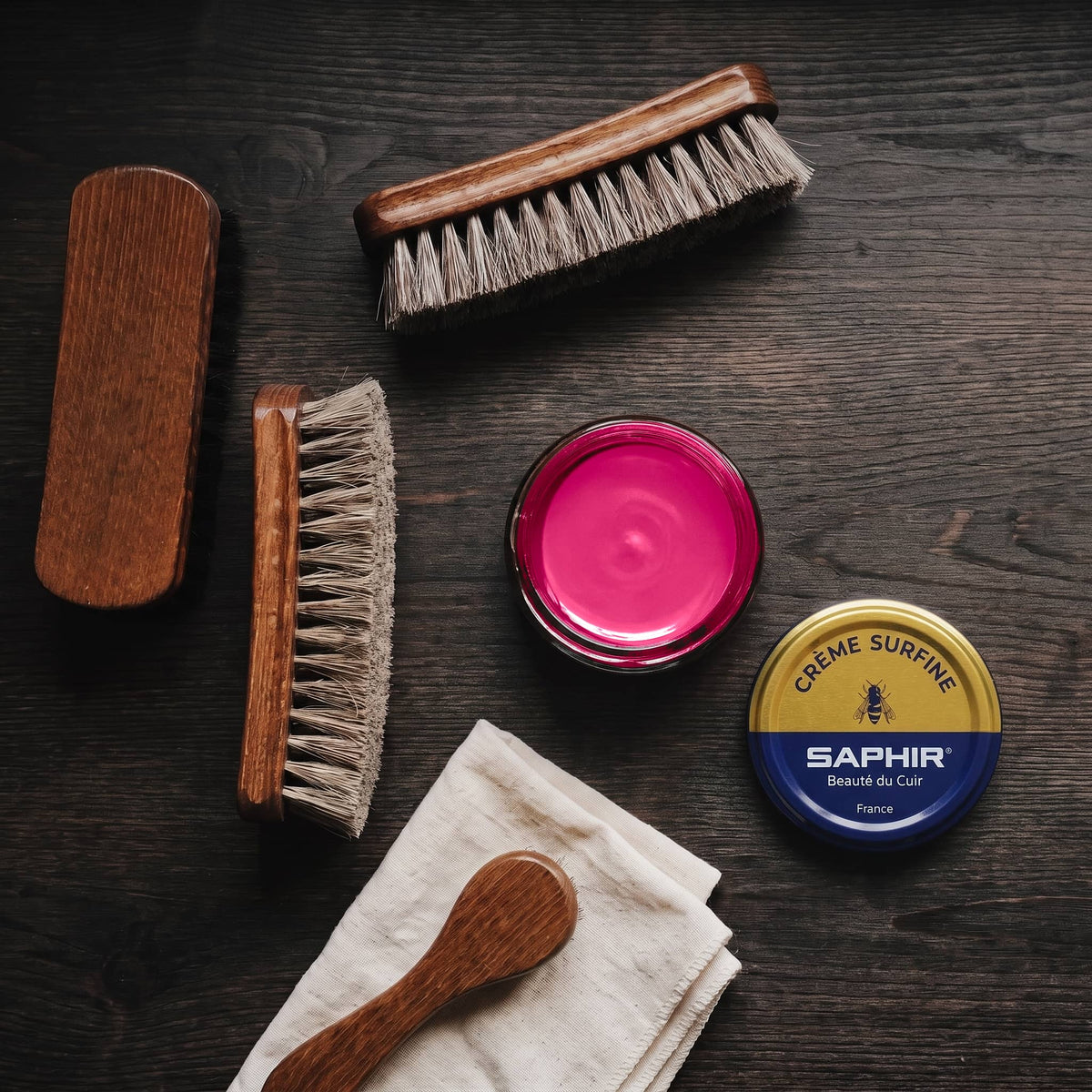 Crème Surfine Saphir Fuchsia en pot ouvert, avec des brosses en crin et une chamoisine, vue de dessus