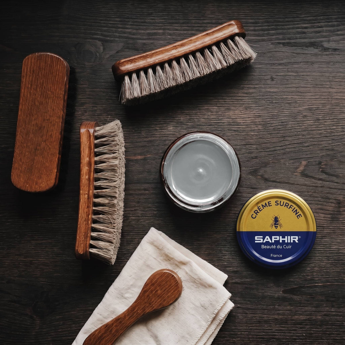 Crème Surfine Saphir Gris en pot ouvert, avec des brosses en crin et une chamoisine, vue de dessus