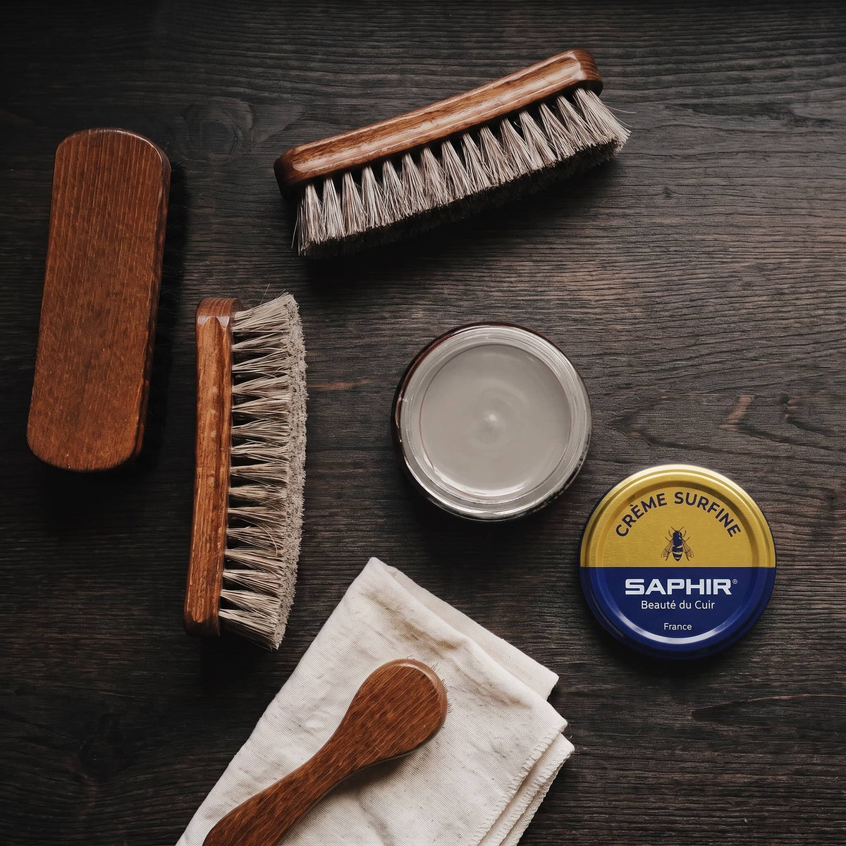 Crème Surfine Saphir Gris taupe en pot ouvert, avec des brosses en crin et une chamoisine, vue de dessus
