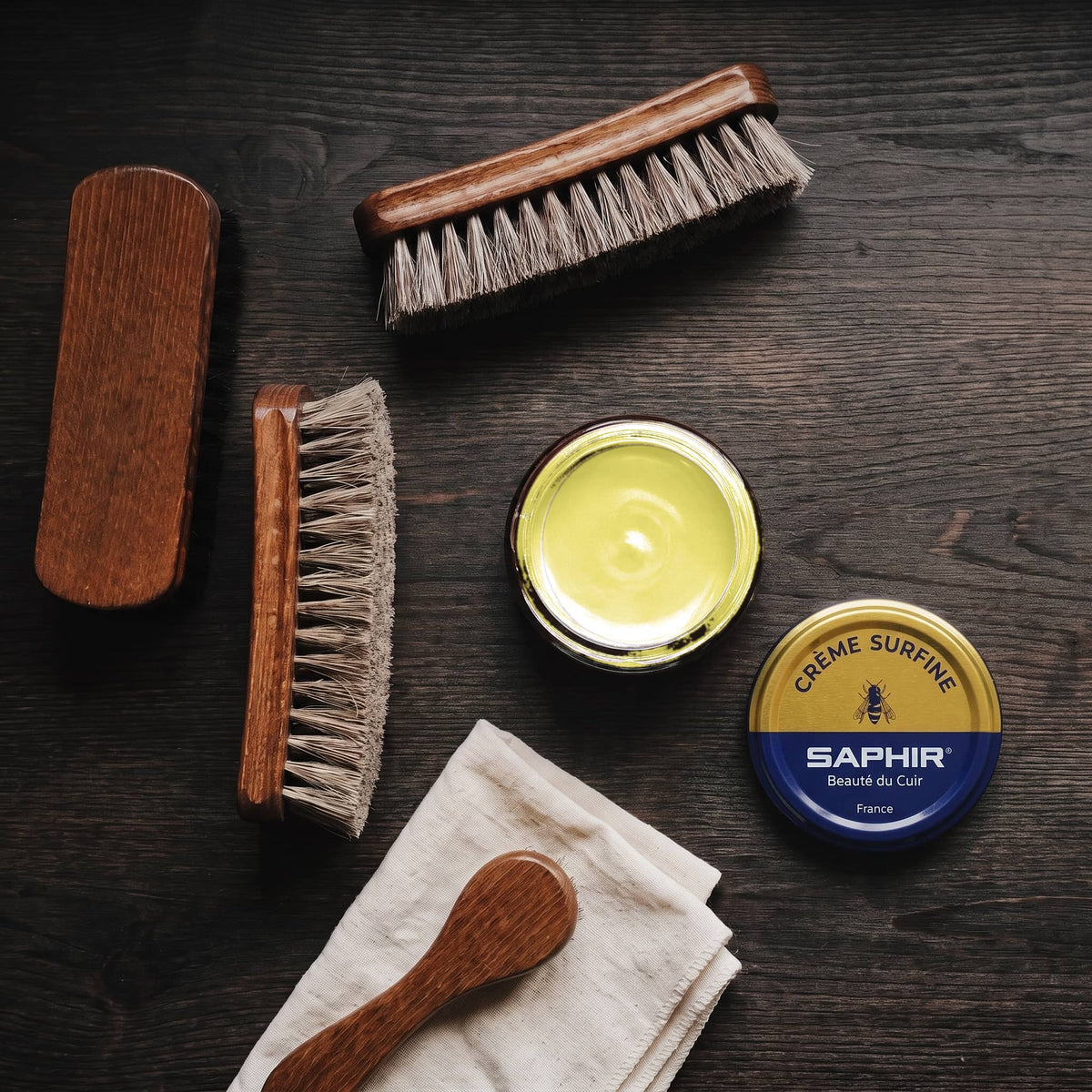 Crème Surfine Saphir Jaune en pot ouvert, avec des brosses en crin et une chamoisine, vue de dessus