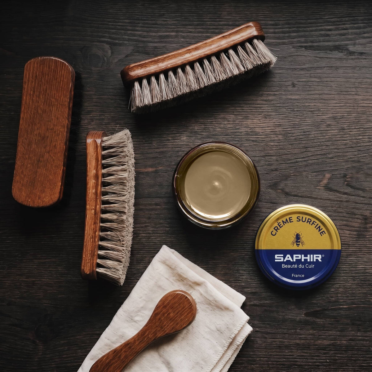 Crème Surfine Saphir Kaki en pot ouvert, avec des brosses en crin et une chamoisine, vue de dessus