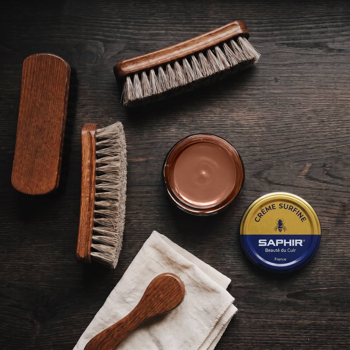 Crème Surfine Saphir Marron moyen en pot ouvert, avec des brosses en crin et une chamoisine, vue de dessus