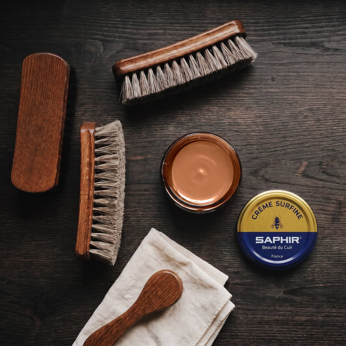 Crème Surfine Saphir Noisette en pot ouvert, avec des brosses en crin et une chamoisine, vue de dessus
