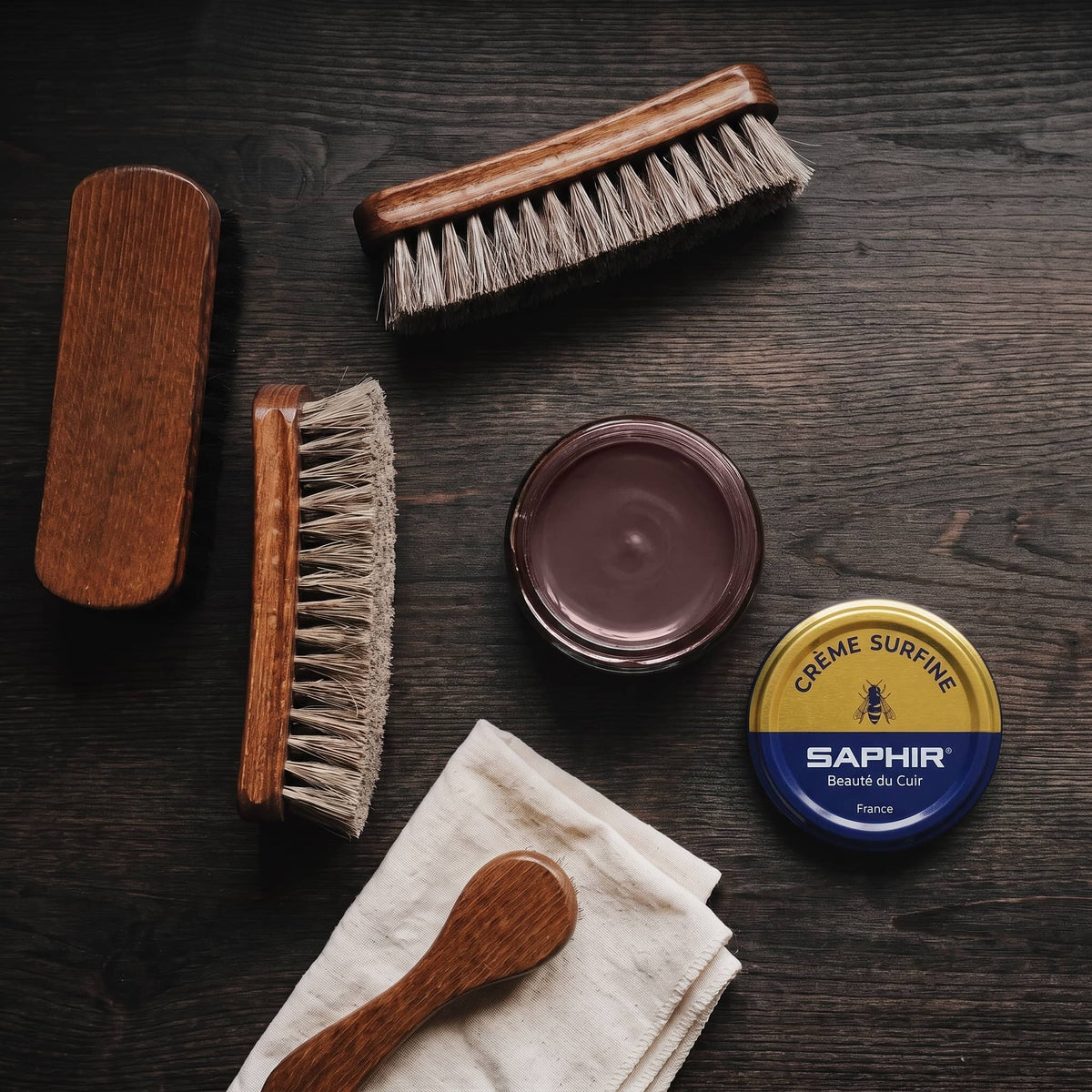 Crème Surfine Saphir Prune en pot ouvert, avec des brosses en crin et une chamoisine, vue de dessus