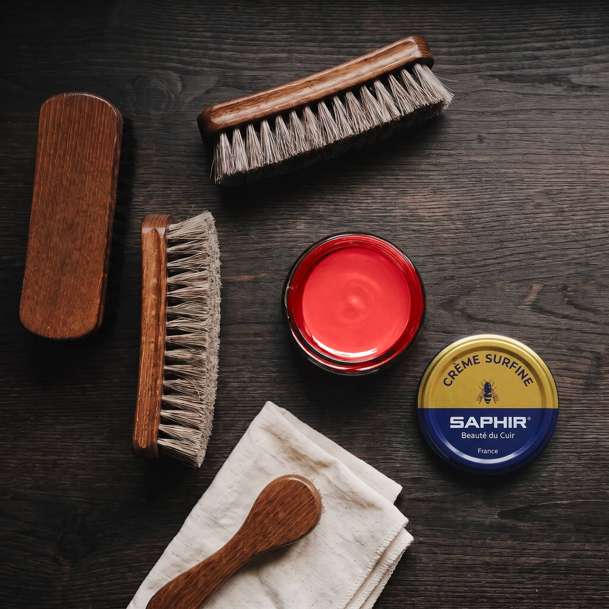Crème Surfine Saphir Rouge en pot ouvert, avec des brosses en crin et une chamoisine, vue de dessus
