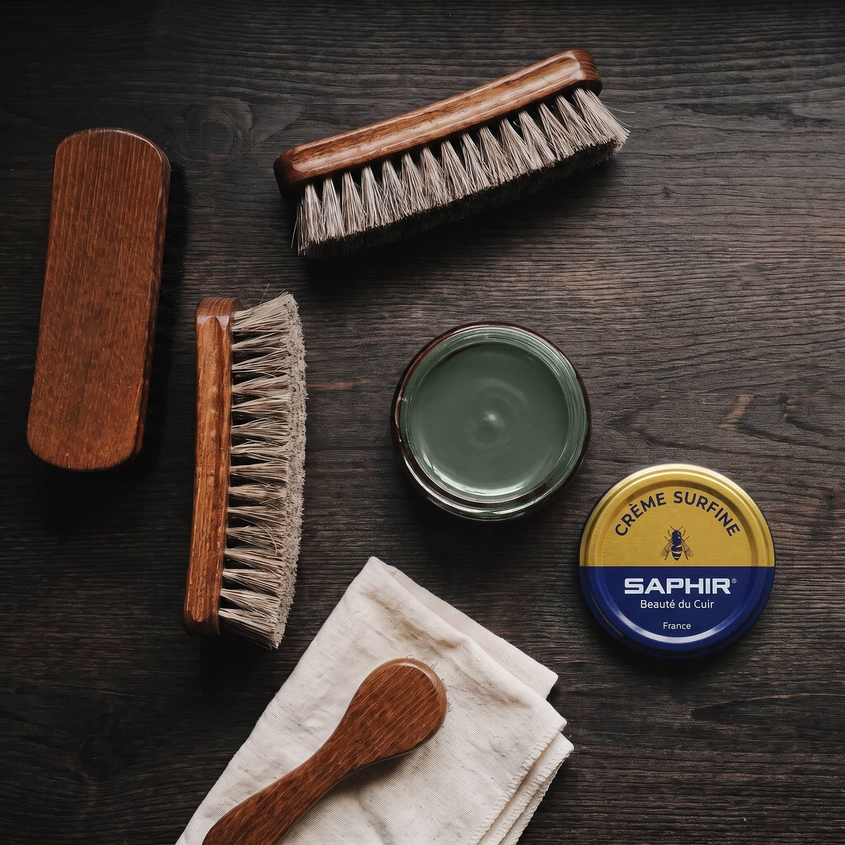 Crème Surfine Saphir Vert Chasse en pot ouvert, avec des brosses en crin et une chamoisine, vue de dessus