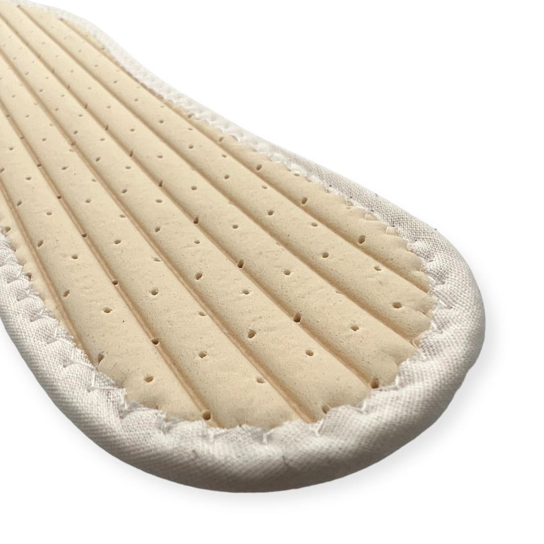 Dessous d’une semelle pieds nus : une mousse beige creusée de canaux et percée de petits trous.